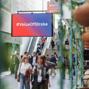 visual from ESOC 2025, hallway with people moving and large screen displaying #VoiceOfStroke