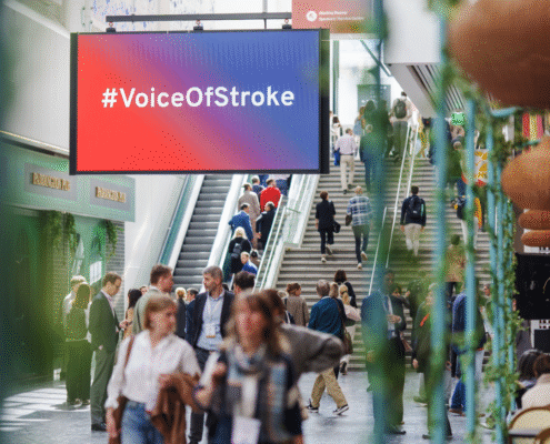 visual from ESOC 2025, hallway with people moving and large screen displaying #VoiceOfStroke